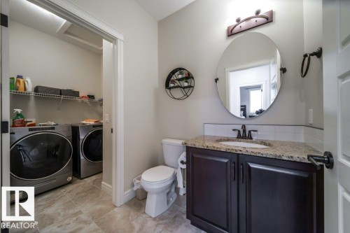 Bathroom featuring a dark wood-finish vanity with a granite countertop, undermount sink, and a round mirror - 3 8050 Orchards Green, Edmonton, AB - Indoor Photo Showing Laundry Room
