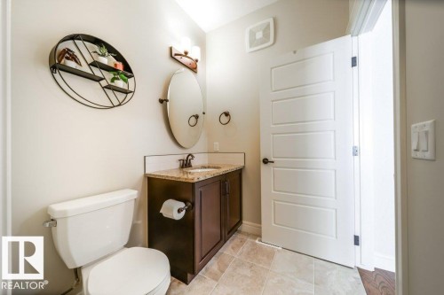 Bathroom featuring a dark wood-finish vanity with a light-colored countertop, an oval mirror, and a contemporary light fixture - 3 8050 Orchards Green, Edmonton, AB - Indoor Photo Showing Bathroom