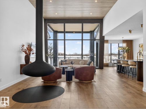 Spacious living area featuring a suspended fireplace, soaring ceiling, wood-finish flooring, and expansive windows - 7104 54 Avenue, Beaumont, AB - Indoor Photo Showing Living Room