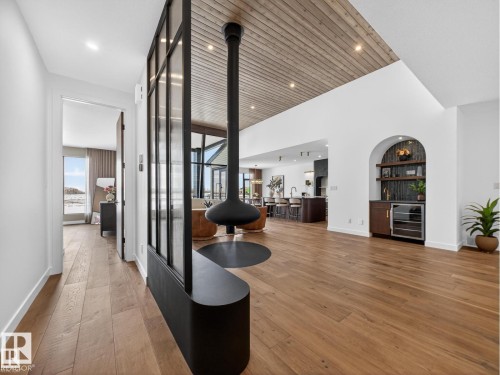Open-concept interior featuring a suspended fireplace, wood-finish flooring, a wood-paneled vaulted ceiling, an arched built-in bar with shelving and beverage cooler, and a glass room divider - 7104 54 Avenue, Beaumont, AB - Indoor Photo Showing Other Room