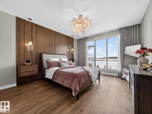 Spacious bedroom featuring wood-finish flooring, a full-height wood accent wall, and a contemporary chandelier - 7104 54 Avenue, Beaumont, AB - Indoor Photo Showing Bedroom