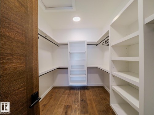 Walk-in closet featuring wood-finish flooring, white built-in shelving, black hanging rods, and recessed ceiling lighting - 7104 54 Avenue, Beaumont, AB - Indoor With Storage