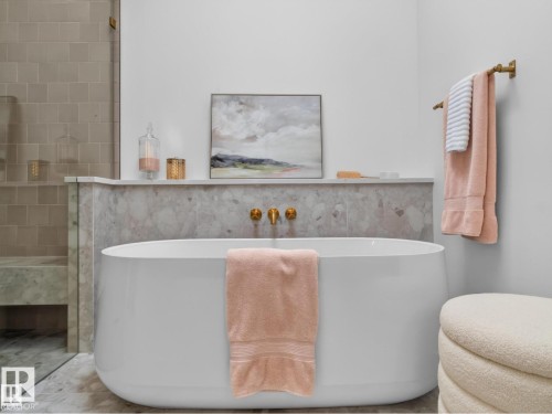 Freestanding soaking tub with wall-mounted brass fixtures, set against a stone-tiled accent wall - 7104 54 Avenue, Beaumont, AB - Indoor Photo Showing Bathroom