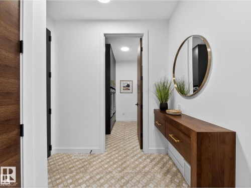 Entryway featuring patterned tile flooring, a floating wood-finish console with brass hardware, and a contemporary round mirror - 7104 54 Avenue, Beaumont, AB - Indoor Photo Showing Other Room