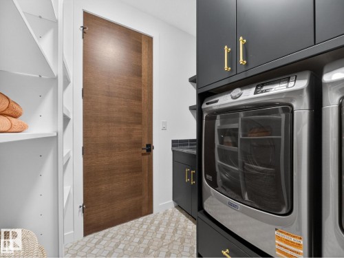 Laundry area featuring stacked appliances, dark cabinetry with gold-tone hardware, and a wood-finish door - 7104 54 Avenue, Beaumont, AB - Indoor Photo Showing Laundry Room
