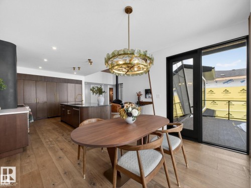 Open-concept dining area featuring wood-finish flooring, a contemporary chandelier, and a dark wood dining table - 7104 54 Avenue, Beaumont, AB - Indoor Photo Showing Dining Room