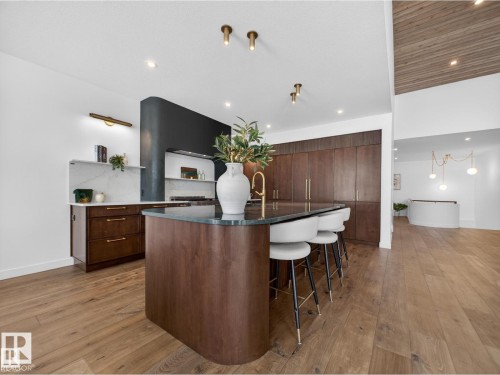 Kitchen featuring a wood-finish island with a dark countertop and gold-finish faucet, built-in cabinetry, white walls, wood-finish flooring, and a slatted wood-finish ceiling accent - 7104 54 Avenue, Beaumont, AB - Indoor