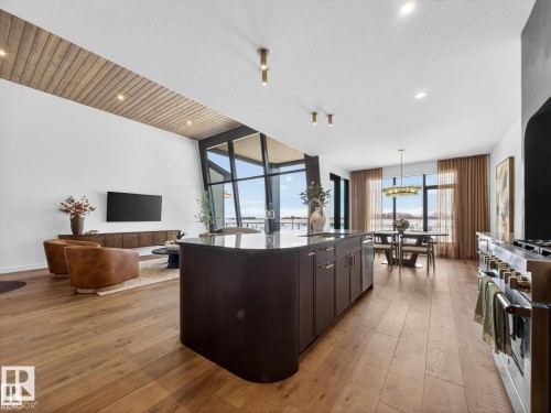 Open-concept living space featuring wood-finish flooring, a kitchen island with stone countertop, stainless steel range, and expansive windows - 7104 54 Avenue, Beaumont, AB - Indoor