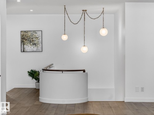 Curved interior wall with a dark wood-finish handrail, contemporary chain-hung pendant lighting with three spherical globes, and wood-finish flooring - 7104 54 Avenue, Beaumont, AB - Indoor Photo Showing Other Room