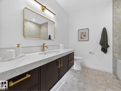 Modern bathroom featuring a dark wood vanity with gold hardware, a white countertop, and an undermount sink with a gold faucet - 7104 54 Avenue, Beaumont, AB - Indoor Photo Showing Bathroom