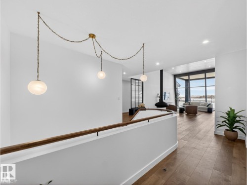 Upper level landing with a modern brass chain pendant light fixture, wood-finish flooring, a curved white railing, and recessed lighting - 7104 54 Avenue, Beaumont, AB - Indoor Photo Showing Other Room