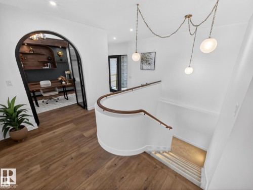 Upper-level landing featuring wood-finish flooring, a curved staircase with wood handrails, and a modern multi-pendant lighting fixture - 7104 54 Avenue, Beaumont, AB - Indoor Photo Showing Other Room