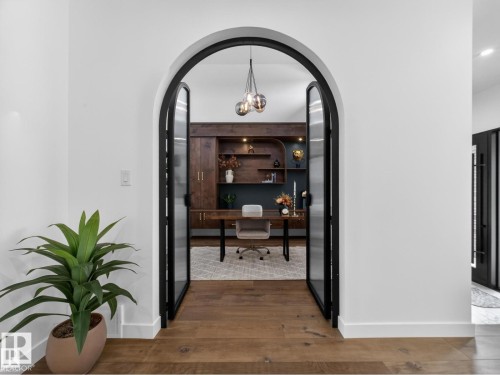 Arched entryway with black-framed glass doors opens to an office space featuring built-in wood cabinetry, a dark accent wall, and a modern chandelier - 7104 54 Avenue, Beaumont, AB - Indoor Photo Showing Other Room