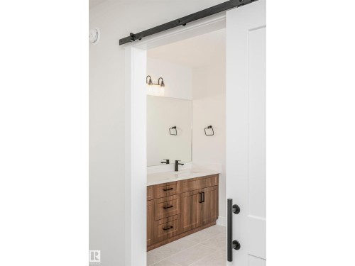 Bathroom featuring a wood-finish vanity with a light-colored countertop, a rectangular mirror, and matte black fixtures - 6302 Dansereau Crescent, Beaumont, AB - Indoor