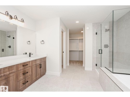 Spacious bathroom featuring a dual vanity with wood-finish cabinetry, a large frameless glass shower enclosure, a built-in tub, and light-toned tile flooring - 6302 Dansereau Crescent, Beaumont, AB - Indoor Photo Showing Bathroom