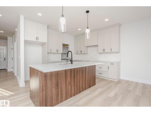 Contemporary kitchen featuring a central island with wood-finish paneling, white countertop, and integrated sink with a matte black faucet - 6302 Dansereau Crescent, Beaumont, AB - Indoor Photo Showing Kitchen