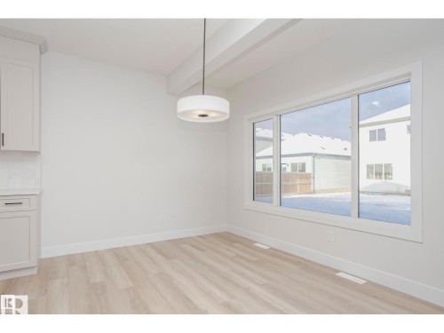 Bright interior space featuring light wood-finish flooring, white baseboards, and a large window with white framing - 6302 Dansereau Crescent, Beaumont, AB - Indoor Photo Showing Other Room
