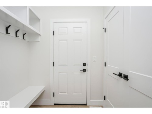 Entryway featuring a white paneled door, built-in bench, built-in shelving, matte black hooks, and matte black door hardware - 6302 Dansereau Crescent, Beaumont, AB - Indoor Photo Showing Other Room