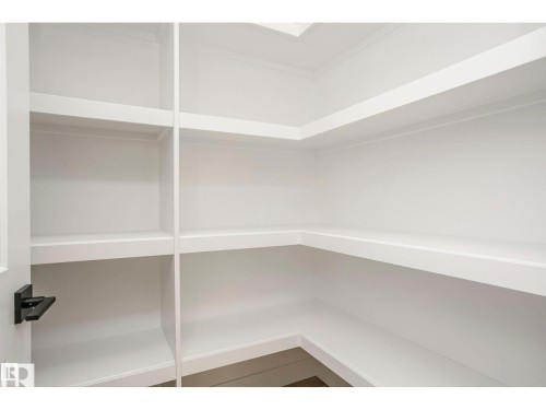 Walk-in pantry featuring extensive white shelving, crown molding, and a modern matte black door handle - 6302 Dansereau Crescent, Beaumont, AB - Indoor With Storage