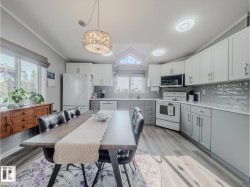 Spacious eat-in kitchen featuring wood-finish flooring, two-tone cabinetry, light countertops, and a tiled backsplash - 