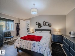 Bedroom featuring wood-finish flooring, a contemporary drum pendant light fixture, a window with exterior visibility, and a paneled interior door - 