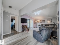 Living area featuring wood-finish flooring, light grey walls, white trim, and a vaulted ceiling - 