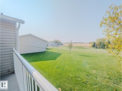 Spacious exterior yard featuring a lush lawn, mature trees, and an expansive field backdrop - 