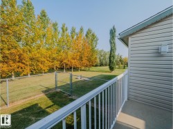 Rear balcony with white railing overlooking a fenced yard and mature deciduous trees - 