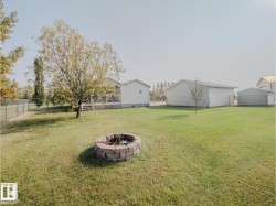 Expansive backyard featuring a stone-lined fire pit, mature trees, chain-link fencing, and a detached white outbuilding - 