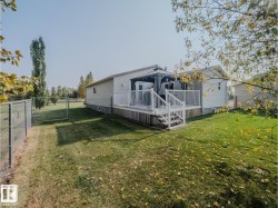Rear exterior featuring a spacious deck with white railings and stairs, a covered gazebo, and a manicured lawn - 