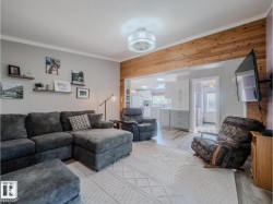 Living area with wood-finish flooring, a decorative ceiling light fixture, and a wood-paneled accent wall - 
