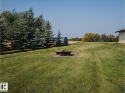 Expansive grassy yard featuring a central fire pit with stone surround - 