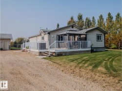 Spacious exterior deck with white railings and an integrated gazebo, complemented by a detached shed, extensive gravel driveway, and surrounding mature trees - 