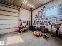 Spacious garage featuring a large roll-up door, concrete flooring, high ceilings with strip lighting, and a wood-burning stove with a visible flue - 
