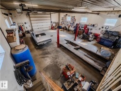 Spacious garage featuring a large overhead door, concrete flooring, multiple windows, and fluorescent lighting fixtures - 