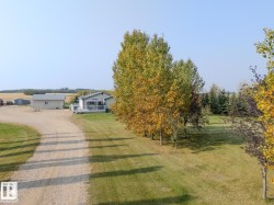 Spacious gravel driveway leading to a single-story residence and detached garage, surrounded by mature trees and expansive green space - 