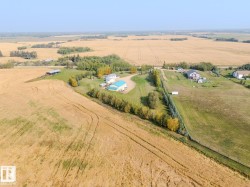 Expansive agricultural landscape featuring a single-family home with a light blue roof, surrounding green spaces, and mature trees - 
