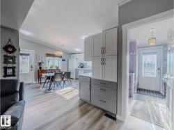 Open-concept living space featuring wood-finish flooring, a dining area with a contemporary light fixture, and a kitchen with white cabinetry and a double-door refrigerator - 