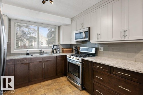 The kitchen features a double basin sink, stainless steel appliances, extensive cabinetry in two tones, and light-colored countertops - 7 Ash Place, St. Albert, AB - Indoor Photo Showing Kitchen With Double Sink
