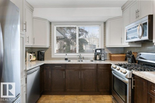 The kitchen features dual-toned cabinetry, stainless steel appliances including a refrigerator, dishwasher, and microwave, and a gas range - 7 Ash Place, St. Albert, AB - Indoor Photo Showing Kitchen With Double Sink