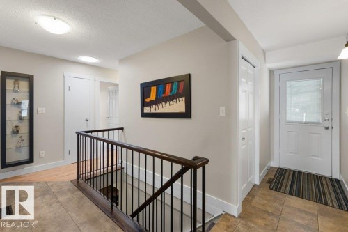 Entryway featuring tile flooring, a white paneled door with a privacy window, and a staircase with dark wood railings and black balusters - 7 Ash Place, St. Albert, AB - Indoor Photo Showing Other Room