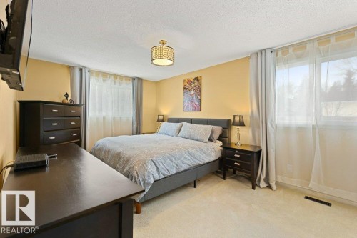 Carpeted room with light yellow walls and two windows, featuring a bed with a gray upholstered frame and a decorative overhead light fixture - 7 Ash Place, St. Albert, AB - Indoor Photo Showing Bedroom