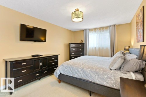 The room features light-colored walls and carpeting, a window with curtains, and a decorative ceiling light fixture - 7 Ash Place, St. Albert, AB - Indoor Photo Showing Bedroom