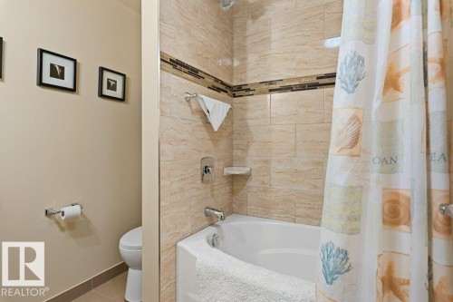 Bathroom featuring a corner bathtub with light-toned tiled walls, a decorative tile accent band, and a white toilet - 7 Ash Place, St. Albert, AB - Indoor Photo Showing Bathroom