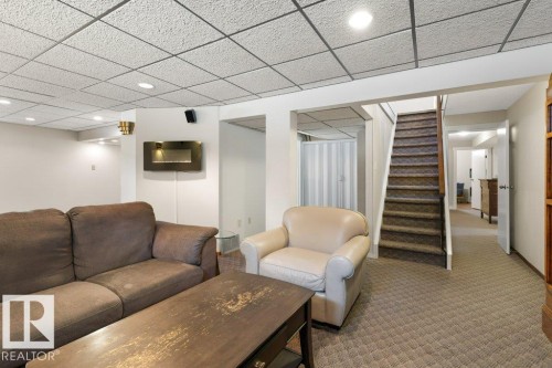 Recreation room featuring recessed lighting, a wall-mounted electric fireplace, and a carpeted staircase with a wooden handrail - 7 Ash Place, St. Albert, AB - Indoor