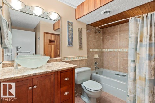 Bathroom featuring a wood vanity with a vessel sink, a mirror with overhead lighting, a tiled tub surround, and a wood plank ceiling accent - 7 Ash Place, St. Albert, AB - Indoor Photo Showing Bathroom
