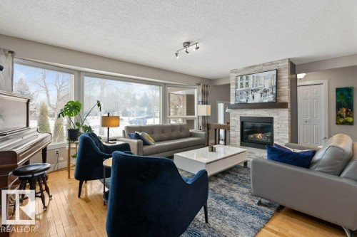 This living area features large windows, hardwood floors, and a fireplace with a stone surround and wood mantel - 7 Ash Place, St. Albert, AB - Indoor Photo Showing Living Room With Fireplace