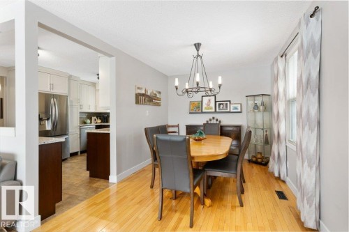 Dining area featuring hardwood flooring and a chandelier, with a view of the kitchen showcasing stainless steel appliances, light-toned cabinetry, and granite countertops - 7 Ash Place, St. Albert, AB - Indoor Photo Showing Dining Room
