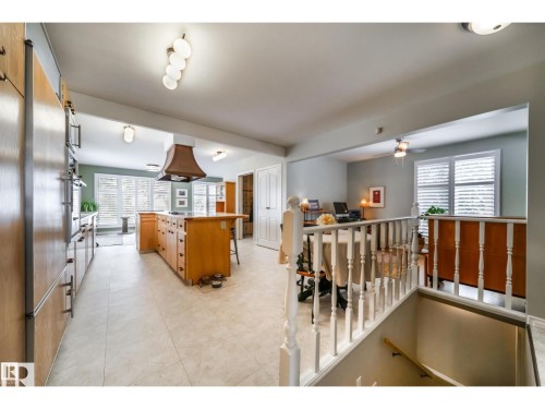 Spacious kitchen featuring a central island with integrated cooktop, warm wood-finish cabinetry, built-in double ovens, and tile flooring - 10231 46 Street, Edmonton, AB 