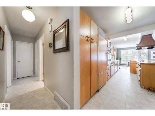 Expansive kitchen featuring light wood cabinetry, integrated refrigerator, double wall ovens, a large island with a cooktop, and a custom range hood - 10231 46 Street, Edmonton, AB 